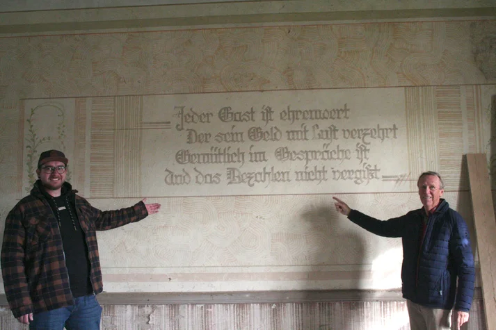 Fabian Froböse und Friedhelm Honig deuten auf einen Spruch an der Wand
