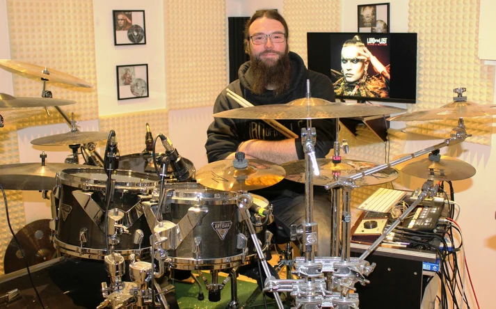 Niklas Kahl sitzt am Schlagzeug, im HIntergrund ist auf einem Monitor das Cover des Lord of the Lost Albums "Blood and Glitter" zu sehen.