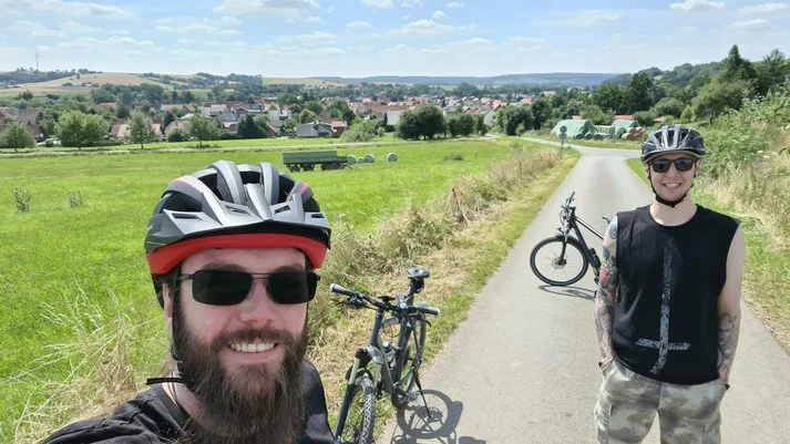 Selfie von Niklas Kahl mit Gerrit Heinemann, im Hintergrund ihre Fahrräder und eine Stadt im Harz.