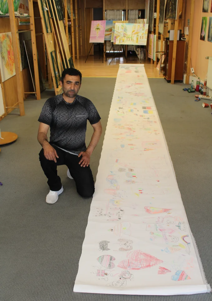 Der Künstler Abdulkarim Alhasan in seiner Galerie mit einem langen Gemälde