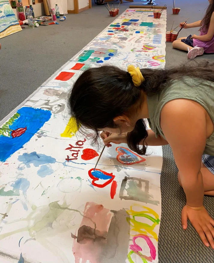 Ein Kind malt auf einer langen weißen Leinwand, welche auf dem Boden liegt