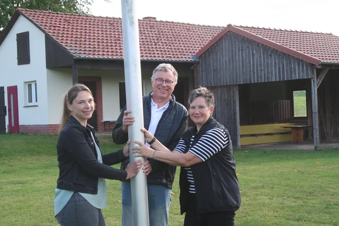 Margitta Kolle (r.), Theo Schmid und Maren Hunger halten einen Pfahl auf einem Sportplatz