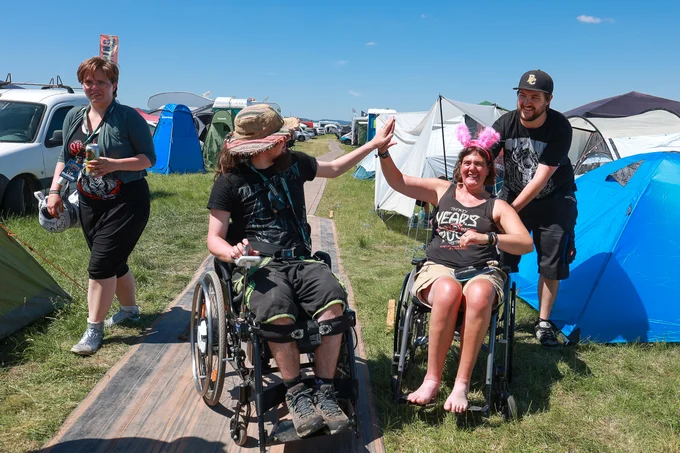 Foto vom Rockharz 2023. Zwei Personen im Rollstuhl auf den Festivalwegen aus ausrangierten Förderbändern
