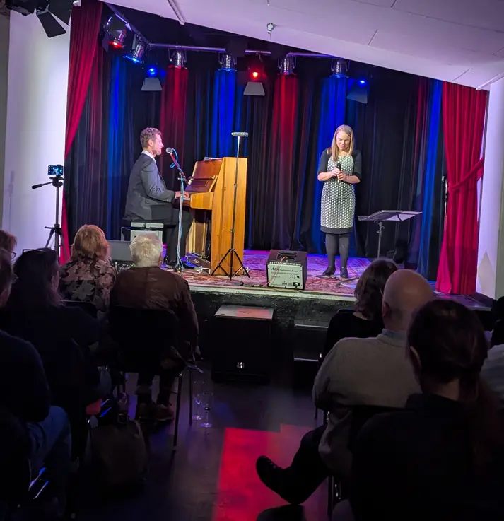 Gregor Kilian am Klavier und Hanna Carlson mit Mikrofon in der Hand auf der Bühne des Apex