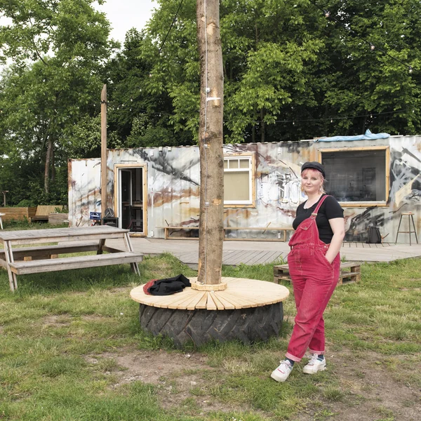 Marlin Helene steht mit überkreuzten Beinen vor einem mit Grafitti besprühtem Container, danaeben mehrere Bäume.