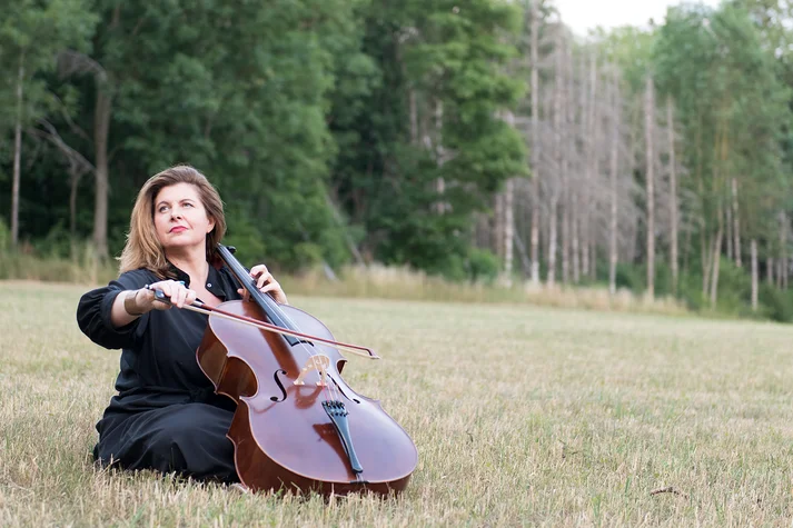 Lucile Chaubard auf einer Wiese sitzend Cello, im Hintergrund ein Nadelwald.