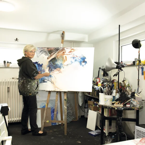 Hiltrud Esther Menz mahlt stehend an einer Staffelei in ihrem Atelier.