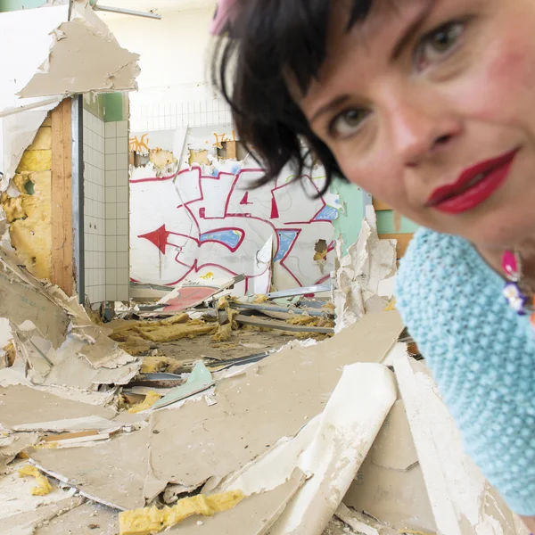 Sonja Elena Schroeder ist unscharf in der oberen rechten Ecke des Bildes zu sehen. Im Hintergrund ist das Innere eines zerstörten und mit Graffitti bemahlten Gebäudes zu sehen.