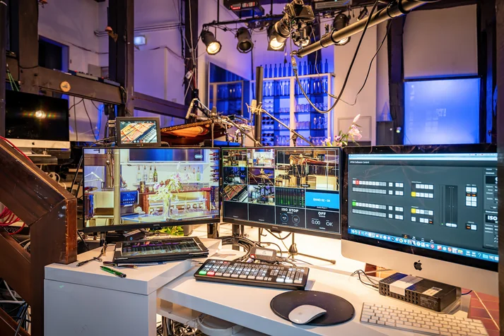 Ein moderner Streamingplatz mit drei Monitoren mit einer Bühne im Hintergrund die sich in einem Fachwerkhaus befindet.
