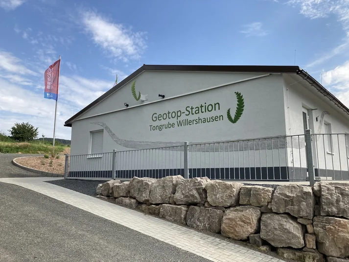 Ein weiß gestrichenes einstöckiges Gebäude, auf dessen Fassade in grüner Schrift "Geotop-Station Tongrube Willershausen" zu lesen ist