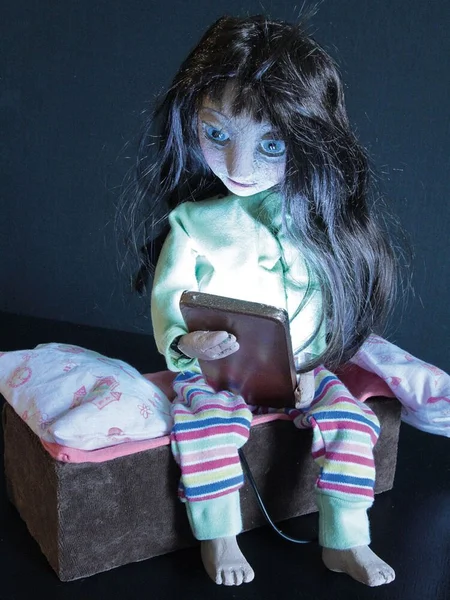 Eine Puppe sitzt auf ihrem Bett und schaut auf ihr Handy