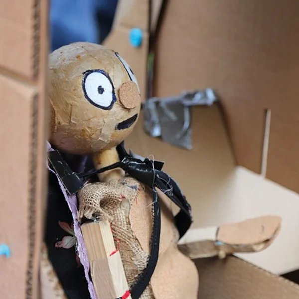 Eine Figur aus Pappmache sitzt in einem Karton