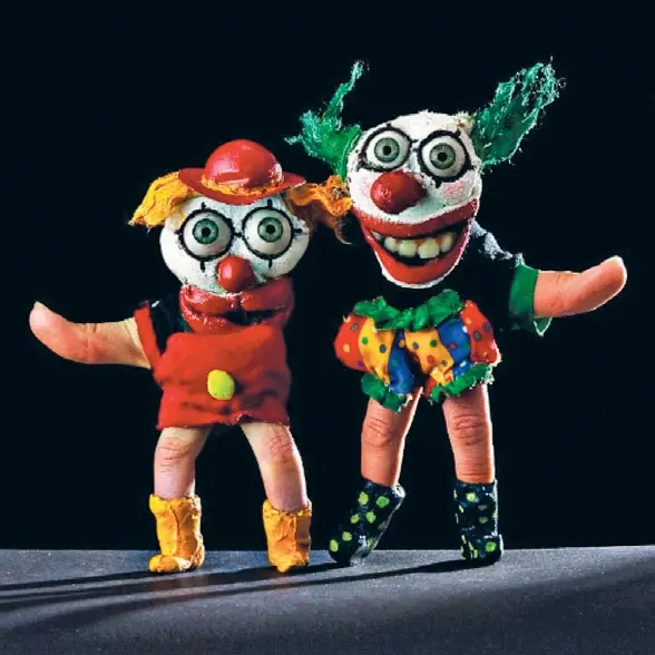 Zwei bunte Fingerpuppen in Clownkostümen stehen nebeneinander. Sie haben große, hervorstehende Augen und breite rote Münder, einer trägt ein rotes Kleid und Hut, der andere eine bunte Hose und grüne Haare.