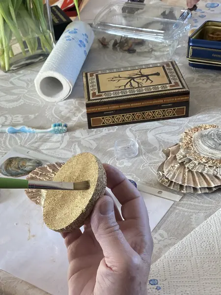 Im Vordergrund ein Korkdeckel, der vergoldet wird und im Hintergrund eine vergoldete Holzschachtel