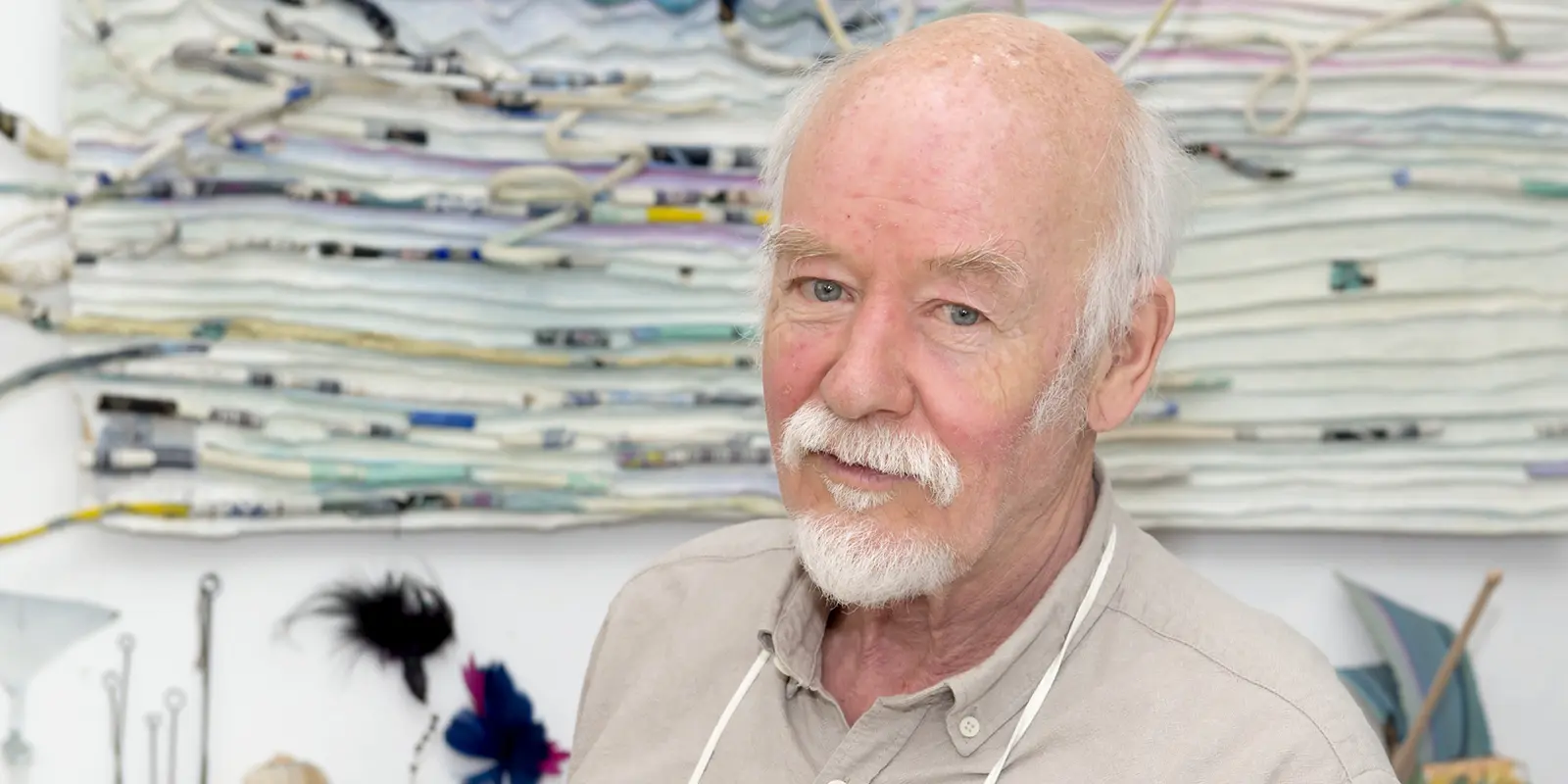 Georg Hoppenstedt steht in seinem Atelier, er trägt eine Malerschürze und blickt mit geneigtem Kopf in die Kamera.