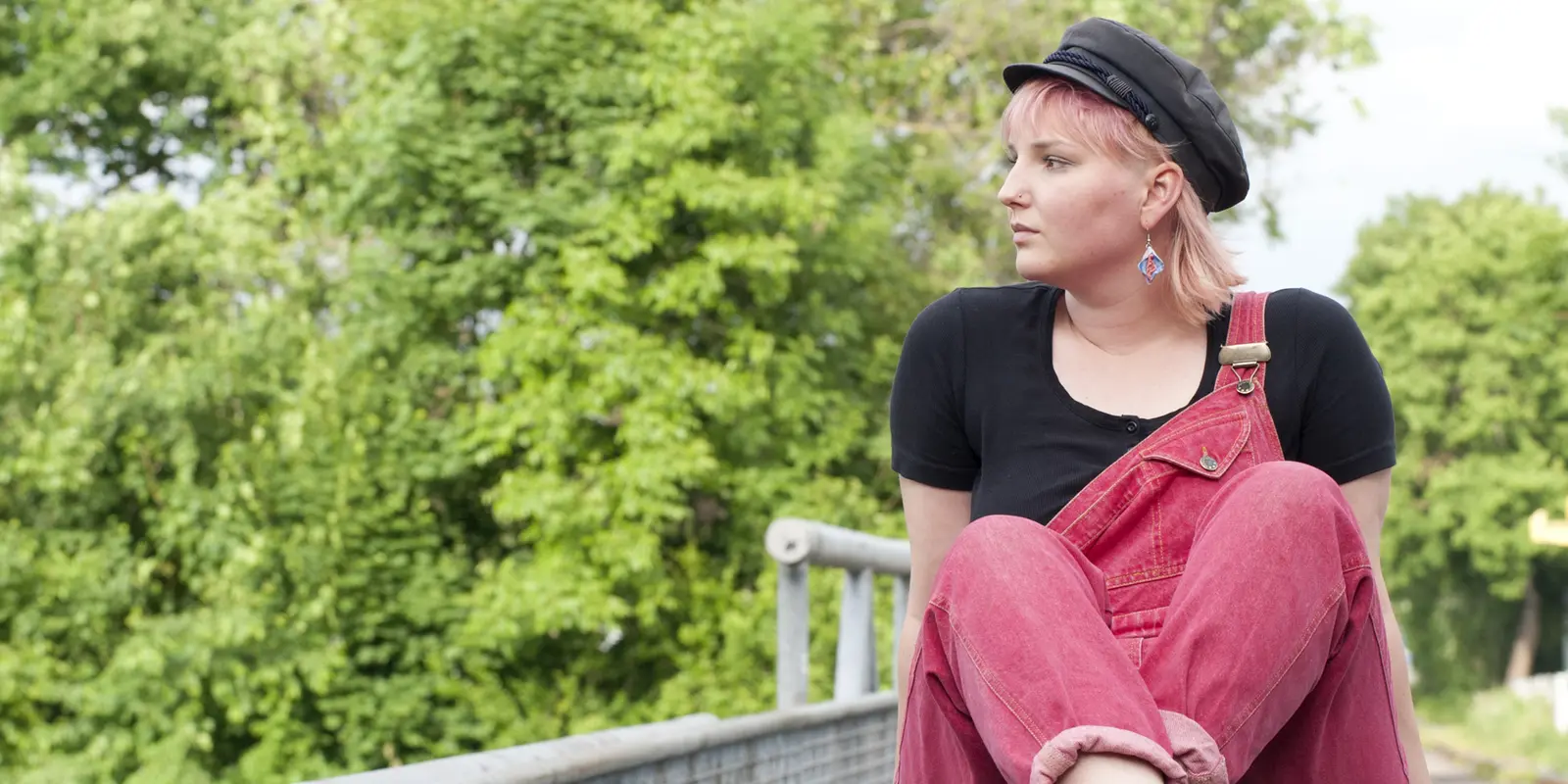 Marlin Helene sitzt mit überkreuzten Beinen auf einer Mauer und schaut in die Ferne.