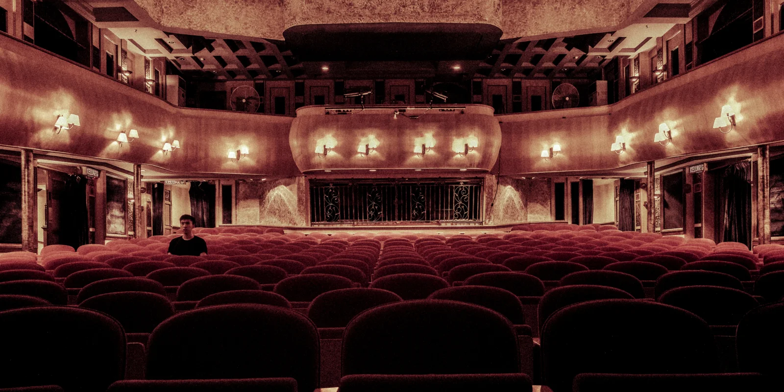 Ein Mann sitzt einsam im Zuschauerraum eines großen Theatersaals.