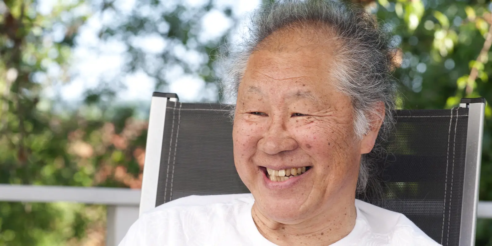Tadashi Endo sitz in einem Gartenstuhl und lacht