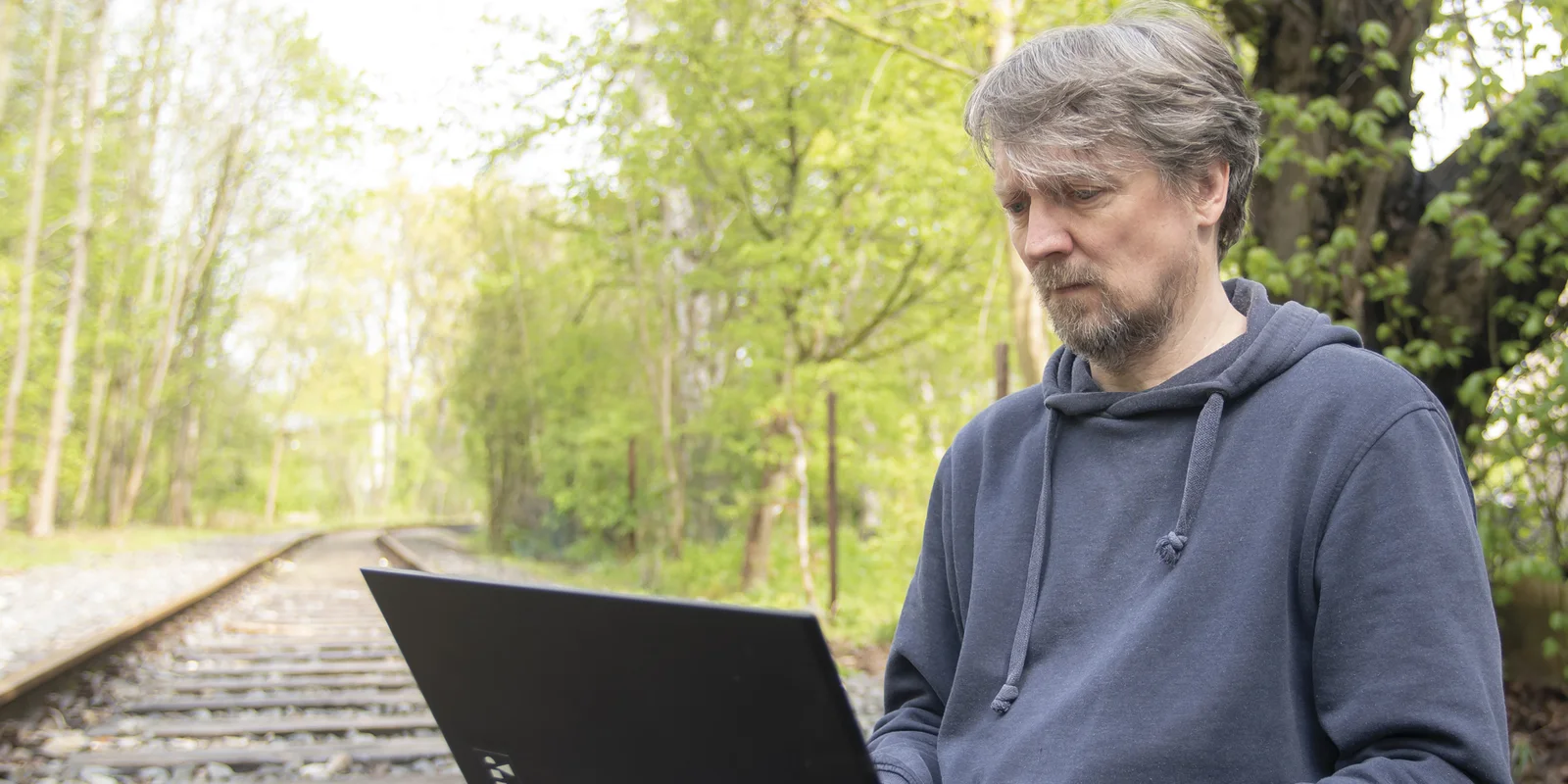 Thomas Kirchberg (alias Tokio) arbeitet auf einer Bahnschiene sitzend an einem Laptop, den er auf seinen Knien stehen hat.