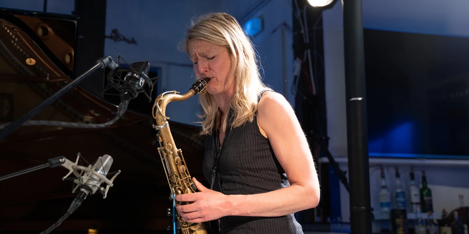 Eine Frau mit blonden haaren und schwarzem Kleid spielt Saxofon