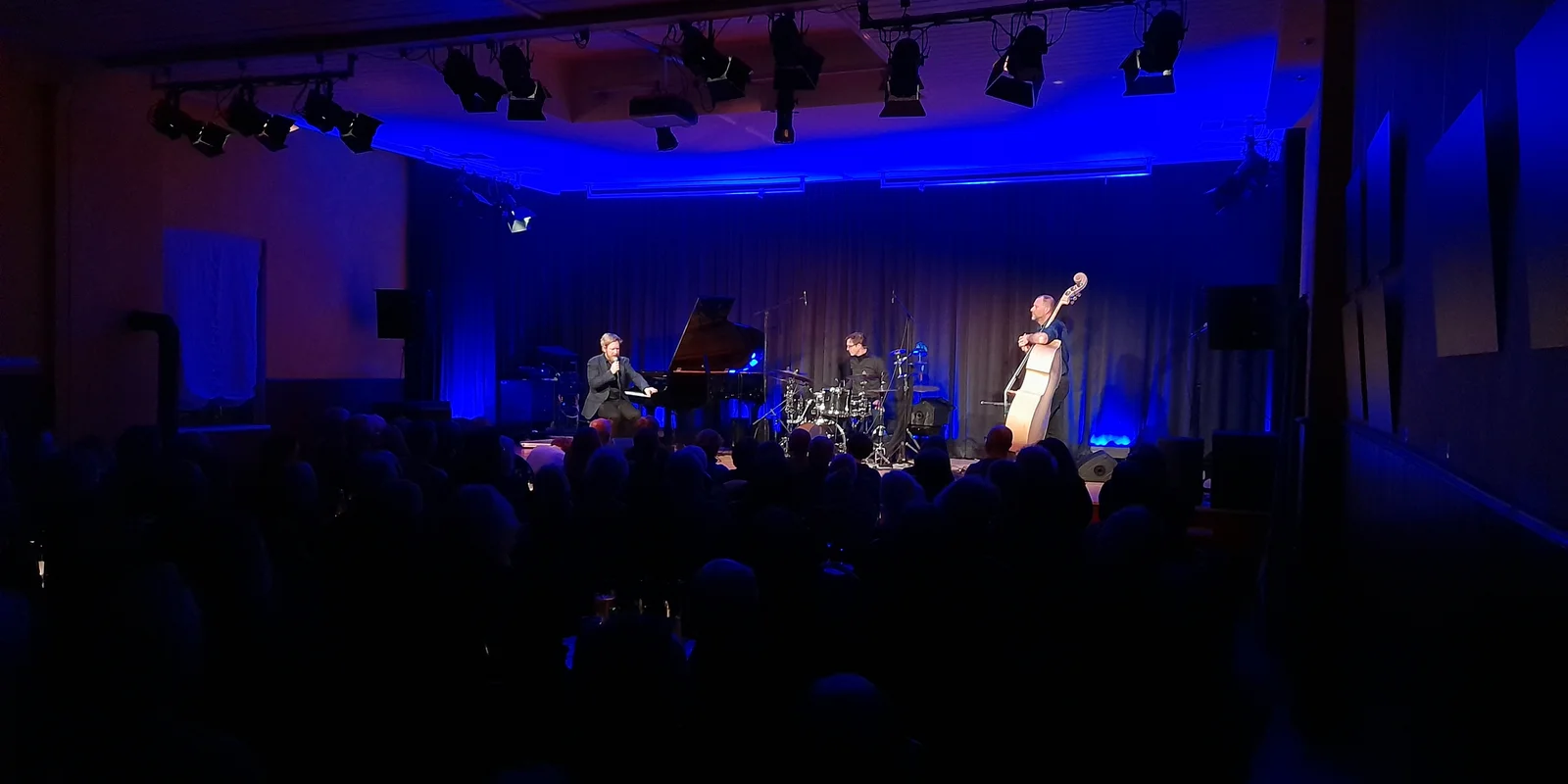 Das Helge Lien Trio, mit Flügel, Schlagzeug und Kontrabass spielt auf der Bühne des Kulturzentrum "Kultur im Esel" im blauen Licht.