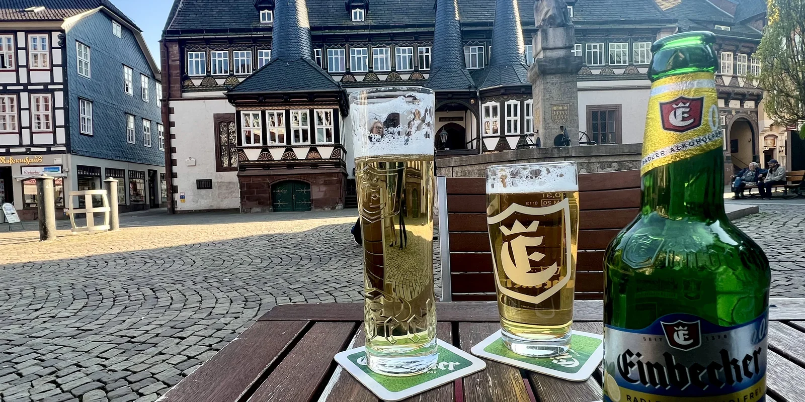 Blick aufs das alte Rathaus Einbeck und den Brunnen auf dem Vorplatz. Im Vordergrund ist eine Flasche Einbecker Radler alkoholfrei und zwei Gläser mit Bier zu sehen.