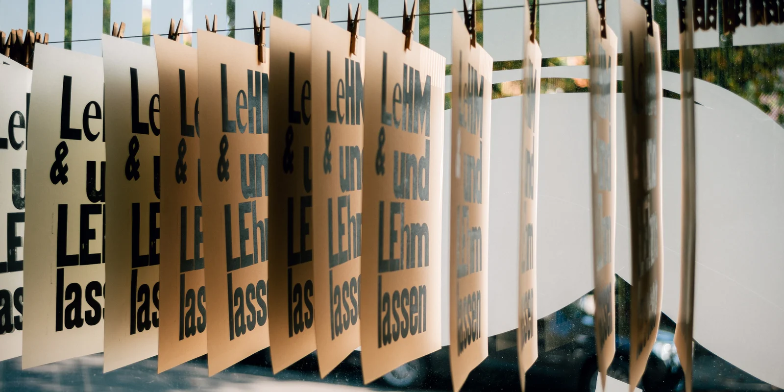 An einer Leine trocknen mehrere gedruckte Postkarten mit der Aufschrift "LeHM und LEhm lassen"