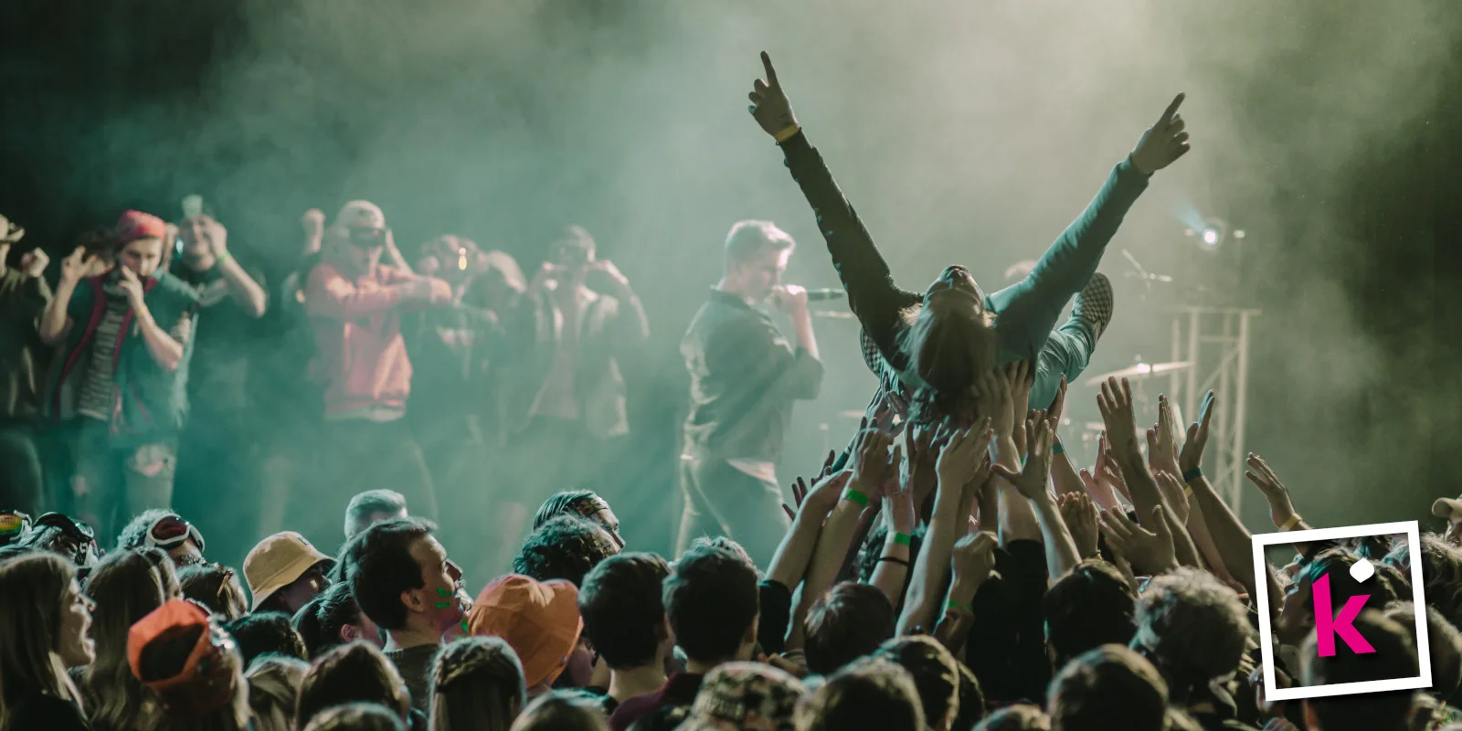 Foto einer Person, die von Konzertbesucher:innen auf Händen getragen wird, im HIntergrund Menschen auf einer Bühne, unten rechts das kulturis-Logo.