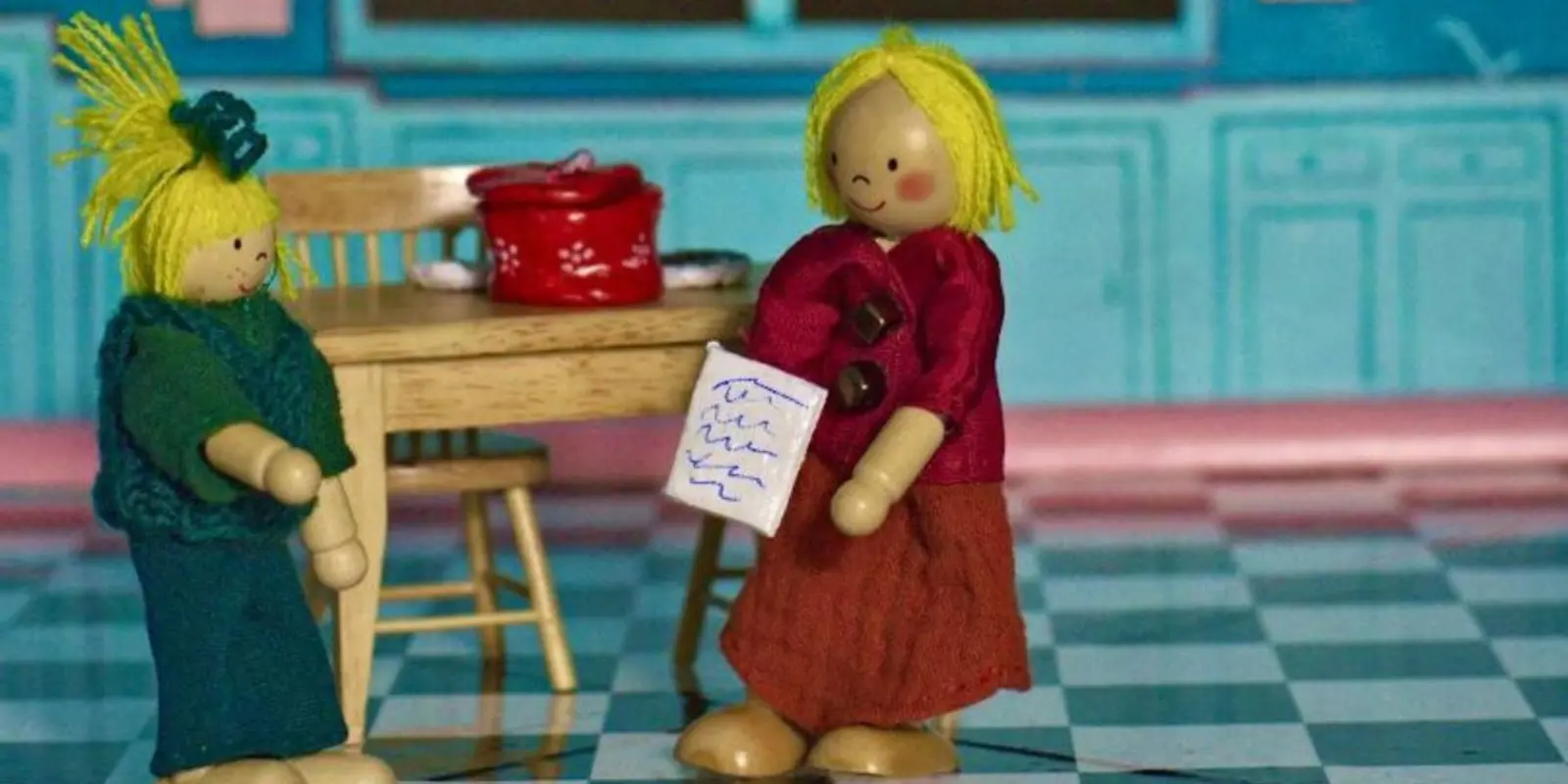 Zwei Spielzeugholzpuppen stehen in einer Küche vor einem Küchentisch