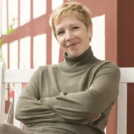 Judith Kara sitzt mit verschränkten Armen auf einer weißen Bank vor einer Fachwerkfassade und lächelt in die Kamera.