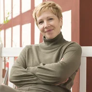 Judith Kara sitzt mit verschränkten Armen auf einer weißen Bank vor einer Fachwerkfassade und lächelt in die Kamera.