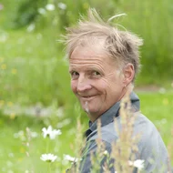 Nik J. Lucht lächelt in die Kamera, er ist umgeben von grünen Pflanzen.
