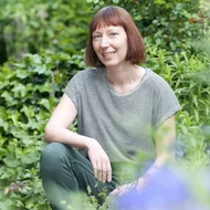 Ruth Reiche kniet in einem Garten und lächelt in die Kamera
