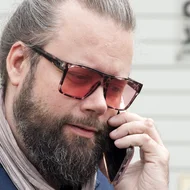 Seitenaufnahme von Tobias Langer, er trägt eine Sonnenbrille und telefoniert mit seinem Smartphone.