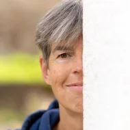 Profilbild Dorothea Heise – sie steht halb verdeckt hinter einer hellen Wand – © Peter Heller