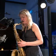 Eine Frau mit blonden haaren und schwarzem Kleid spielt Saxofon