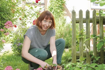 Ruth Reiche kniet in einem Garten und lächelt in die Kamera, ihre Hände sind voller Erde und stecken in einem Blumentopf mit Erdbeeren.