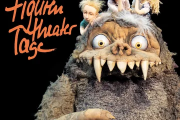 Auf schwarzem Grund links der Schriftzug "Figurentheatertage", daneben eine Monster-Figur mit zotteligem grauen Felld und riesigen Zähnen, auf deren Kopf drei Kinderfiguren sitzen und träumerisch in die Gegend schauen. 