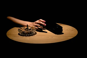 Ein Tisch, darauf ein voller Aschenbecher, von der linken Seite greift eine Hand nach einem Telefonhörer.