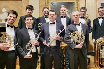 Auf dem Bild sind alle Mitglieder des Blechbläserensembles der AOV zusammen mit ihren Instrumenten in der Aula am Wilhelmsplatz abgebildet.