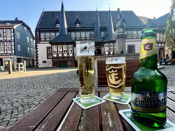 Blick aufs das alte Rathaus Einbeck und den Brunnen auf dem Vorplatz. Im Vordergrund ist eine Flasche Einbecker Radler alkoholfrei und zwei Gläser mit Bier zu sehen.