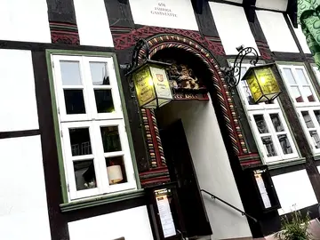 Der Eingang des Fachwerkhaus Brodhaus sowie Tisch und Stühle die davor auf der Straße stehen.