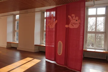 Ausstellungsraum mit einer Installation aus rotem Stoff und darauf abgebildeten Händen