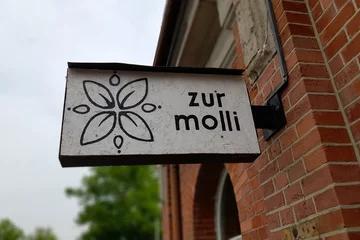 Ein weißes Schild mit der Aufschrift „Zur Molli“ und einer Blume am alten Bahnhof in Salzderhelden