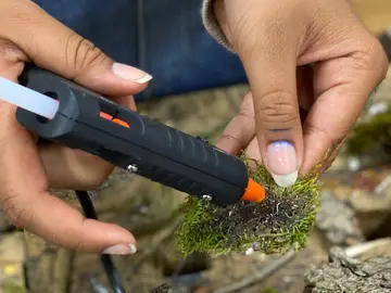 Hände kleben mit einer Heißklebepistole Naturmaterialien zusammen.