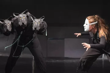 Eine Maskierte Person steht einem Dreiköpfigen Hund gegenüber