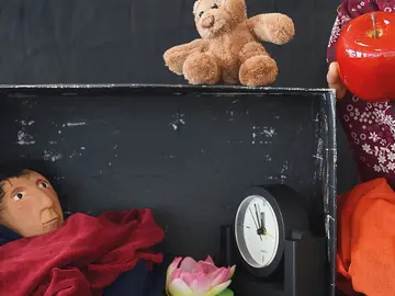 Eine Puppe verkriecht sich in einem Schuhkarton