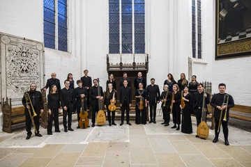 Eine Gruppe Musiker:innen steht schwarz gekleidet in einer weißen Kirche