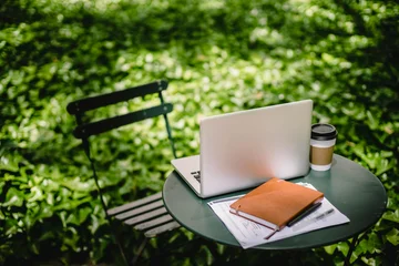 Ein Stuhl, ein Tisch mit Laptop, Buch und Kaffee im Garten