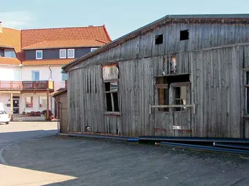 Das Bild eine zerfallenen Holzbaracke vor einem Haus.